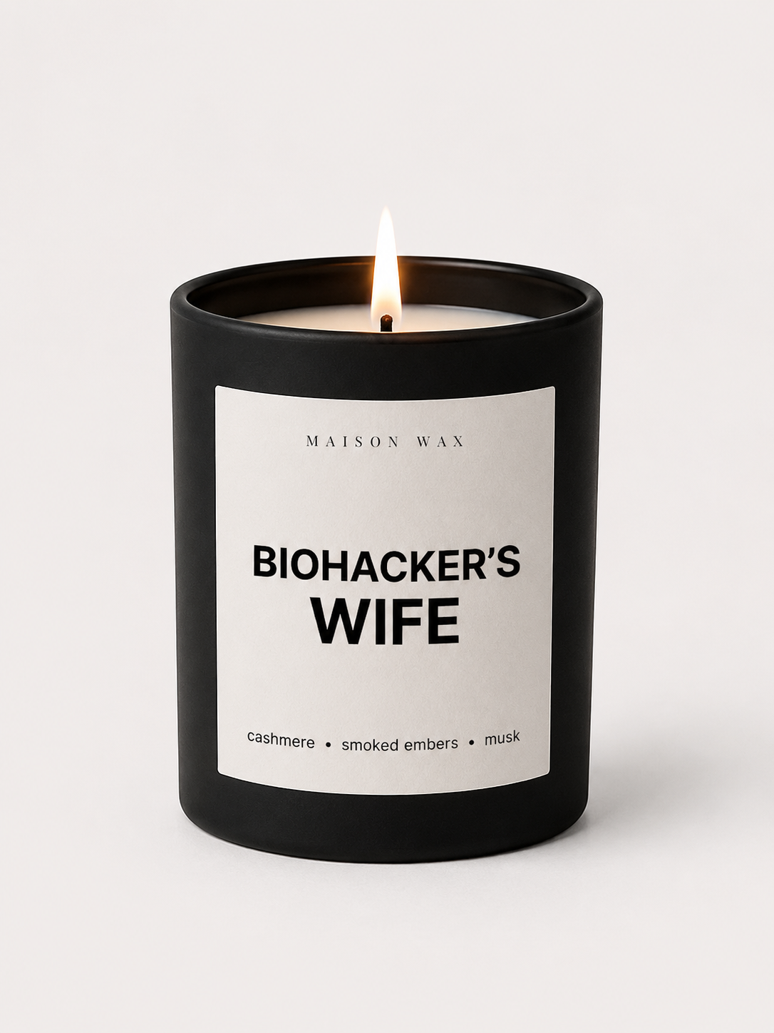 Maison Wax 'Biohacker's Wife' candle, lit, with cashmere, smoked embers, and musk scent notes.